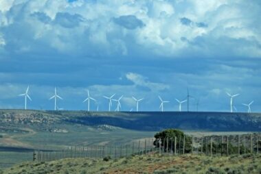Wind turbines in a row on grassy hills with storm clouds moving over them.